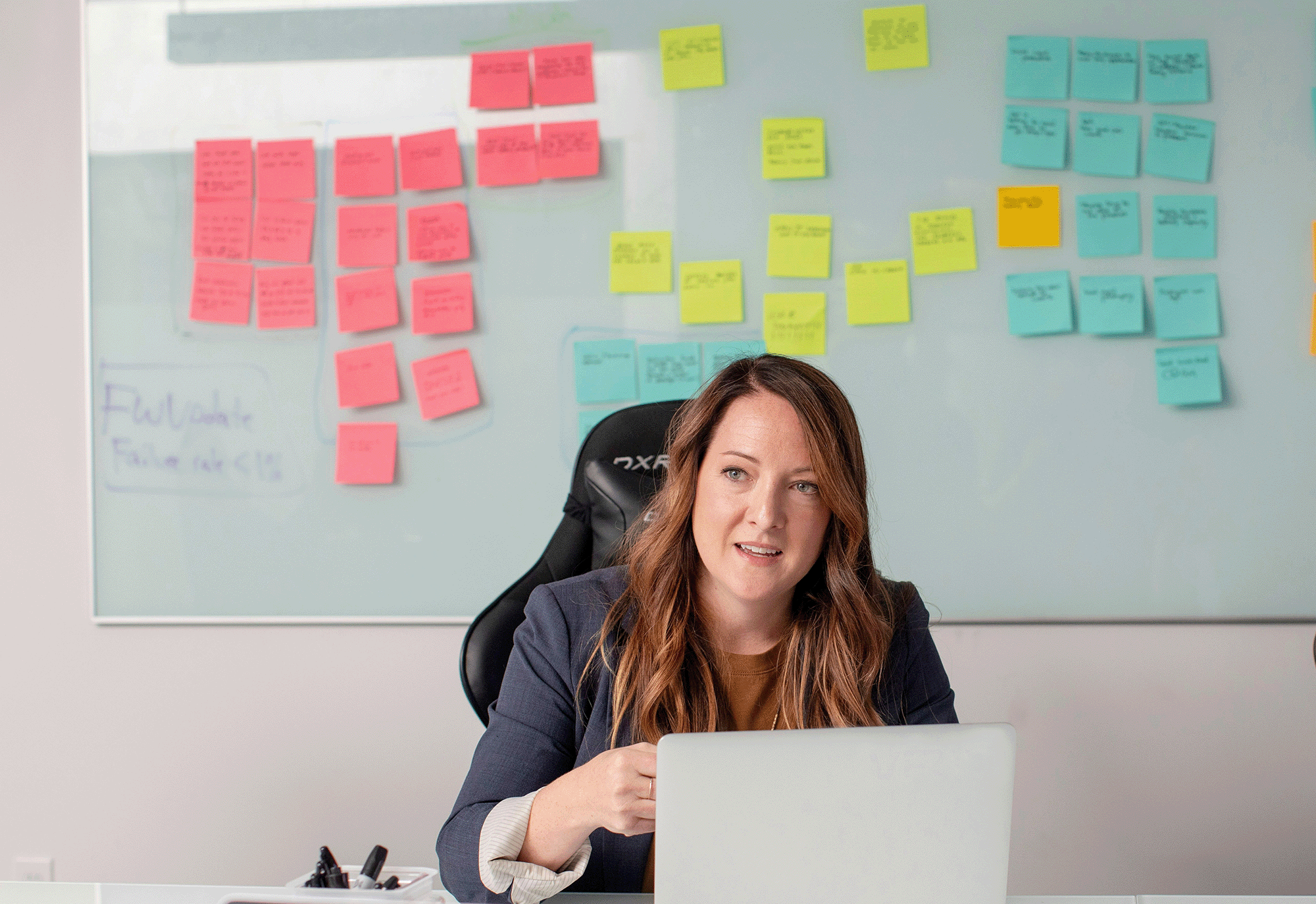 Woman on computer with a system of sticky notes behind her