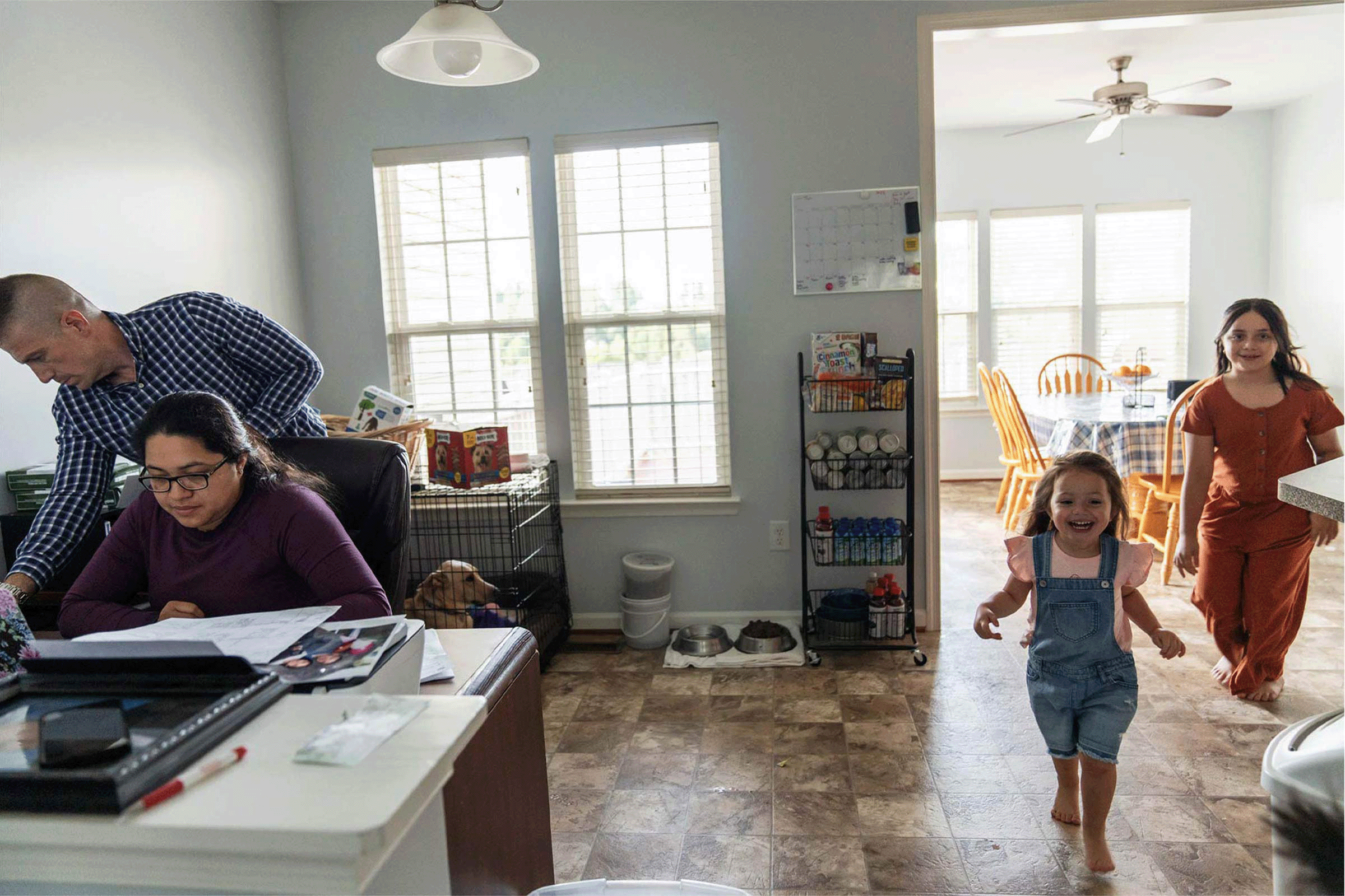 SCPS student and mother working at desk with family busy in her house