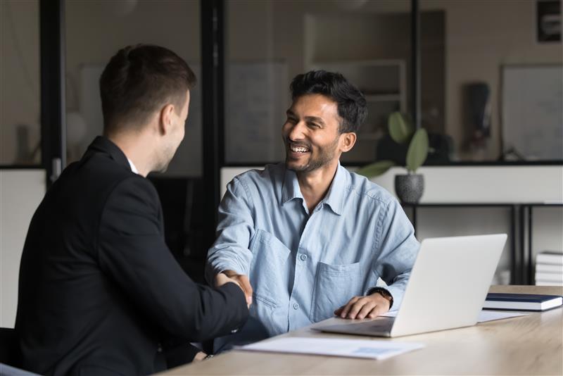 Two male colleagues shake hands in front of a laptop computer