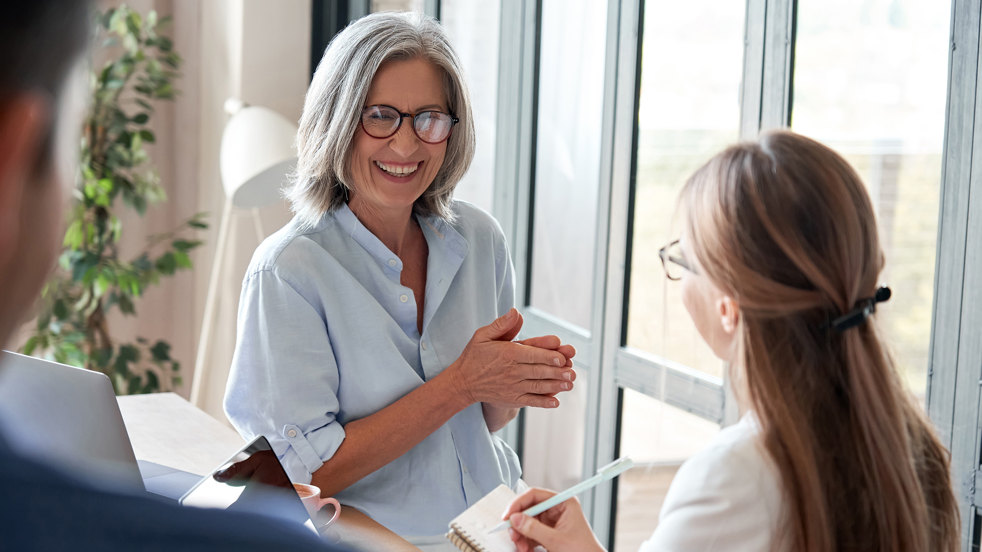 A coach and her mentee are seated. The coach wears glasses and smiles at her mentee