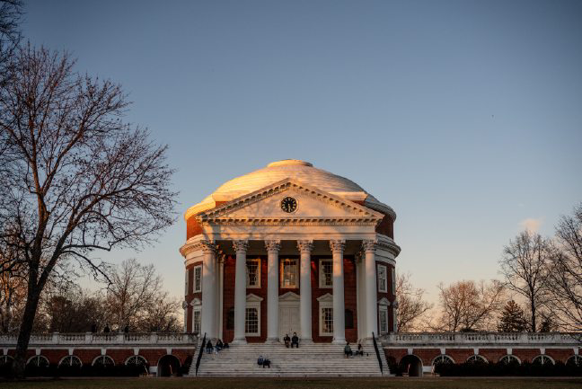 UVA's Rotunda on the Lawn at sunset. Bare trees surround the round, brick building with white pillars.
