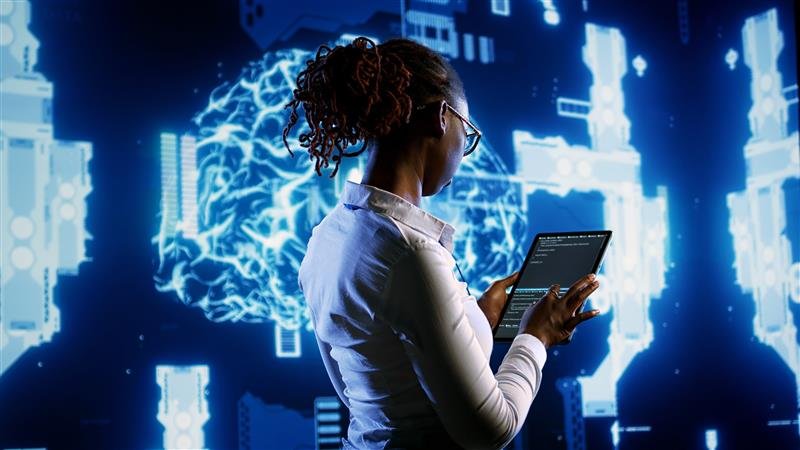 Woman uses AI to program data from her tablet to a large viewscreen.