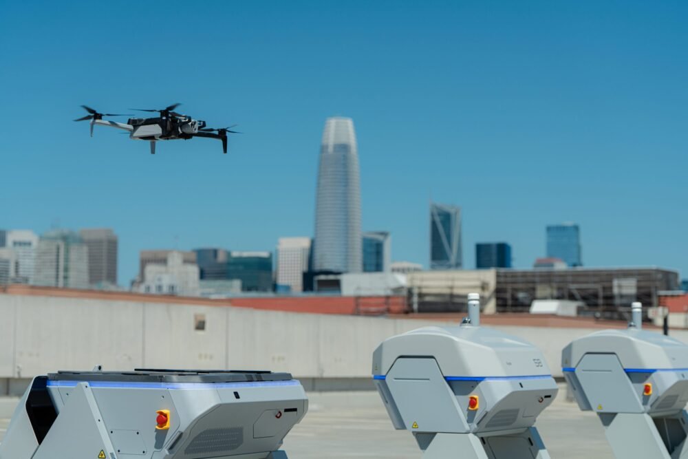 A drone flies in the air with a cityscape behind it