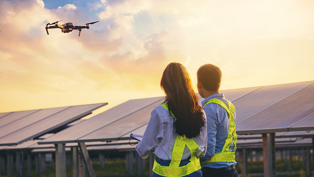 Two drone operators pilot a drone over a solar panel array